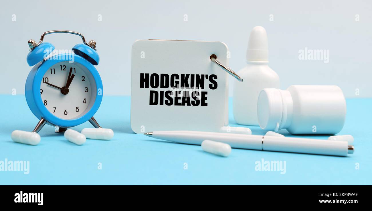 Medicine and health concept. On a blue surface lie pills, an alarm clock and a notebook with the inscription - Hodgkin s disease Stock Photo