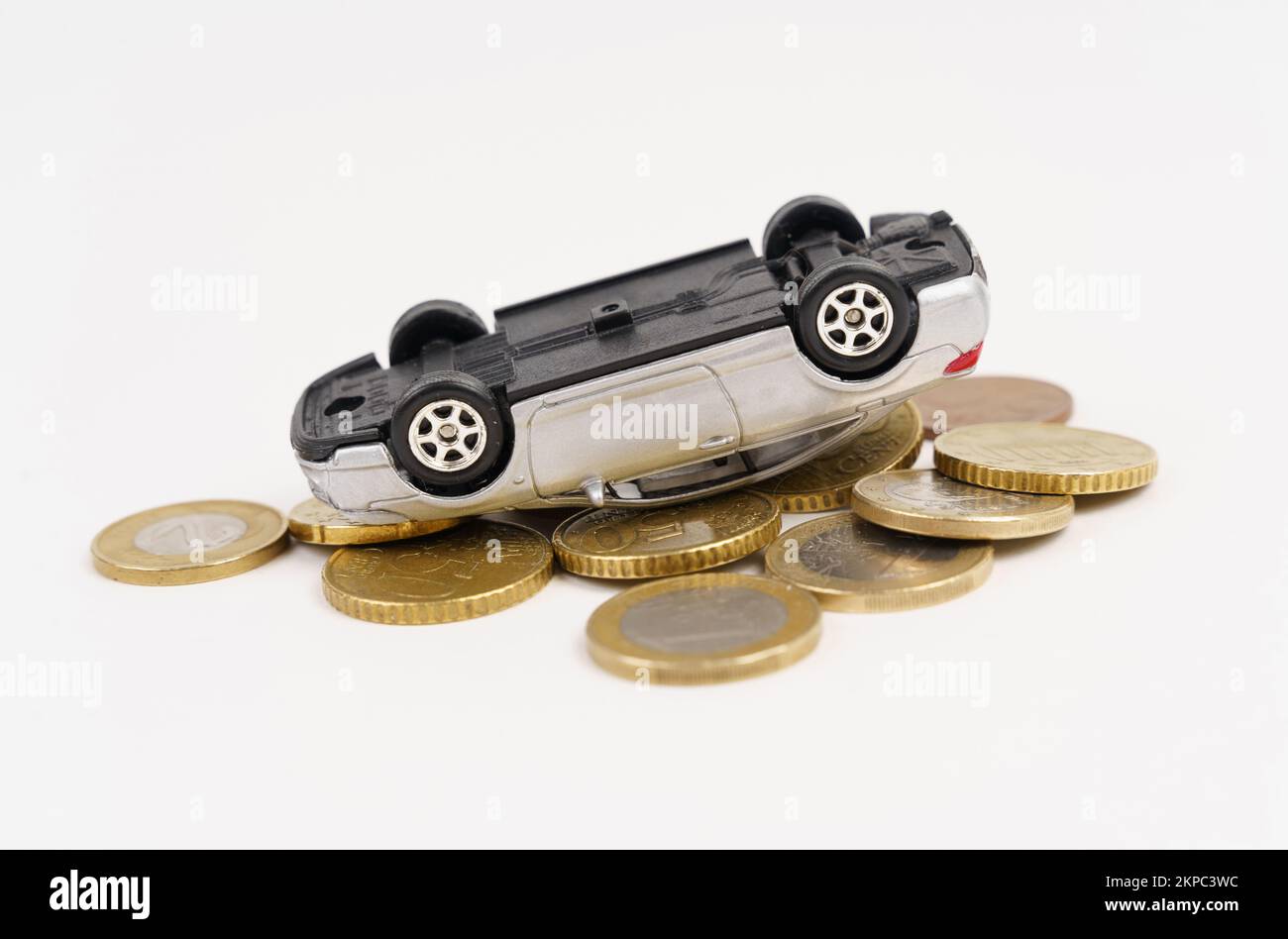 Traffic accident, car insurance concept. The silver car is turned upside down and rests on the coins. Stock Photo