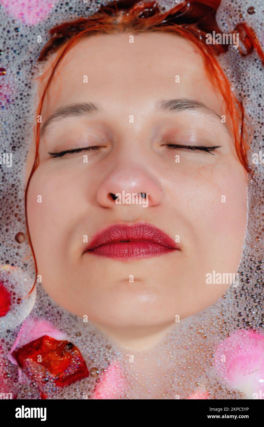 The face of a beautiful woman in bathroom among foam and rose petals Stock Photo