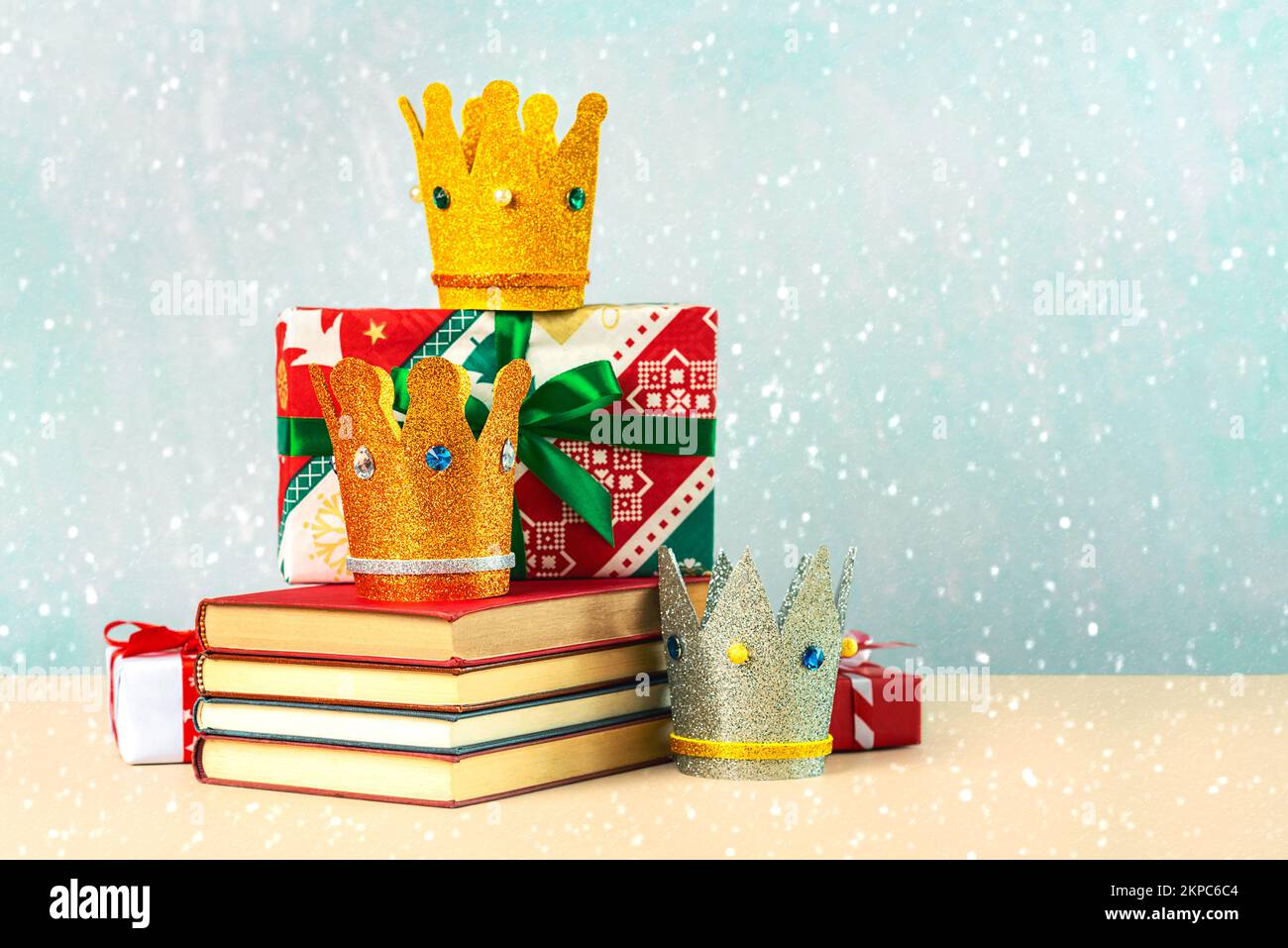 Three crowns of the three wise men with books,christmas gift boxes and snowflakes over blue background Stock Photo
