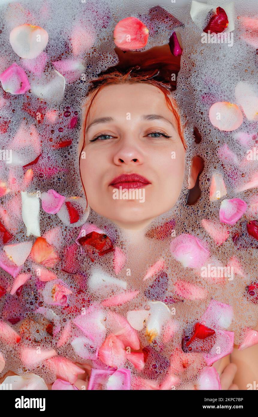 face of a beautiful woman in the bathroom among foam and rose petals Stock Photo