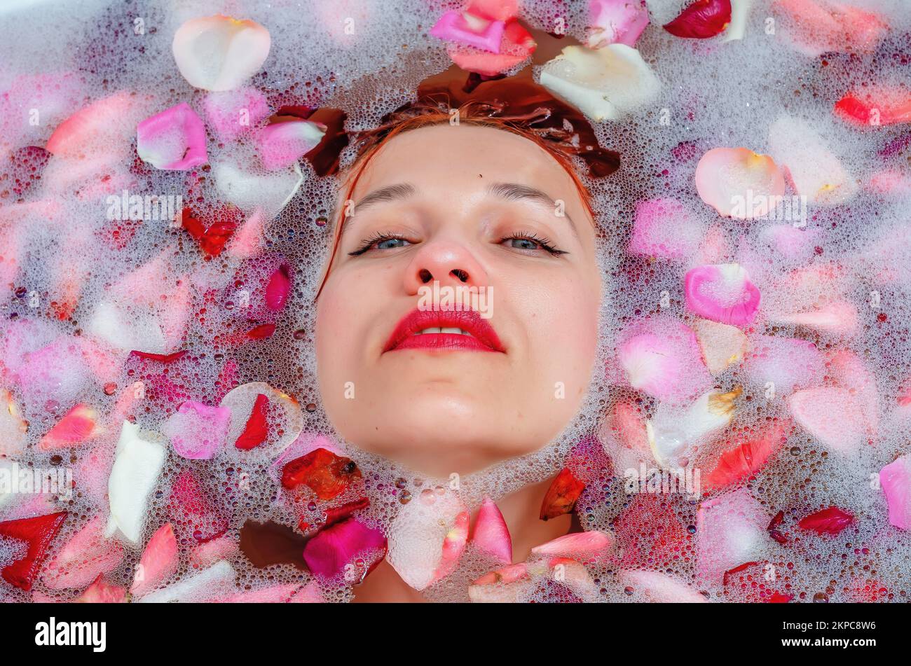 The face of a beautiful woman in the bathroom among foam and rose petals Stock Photo