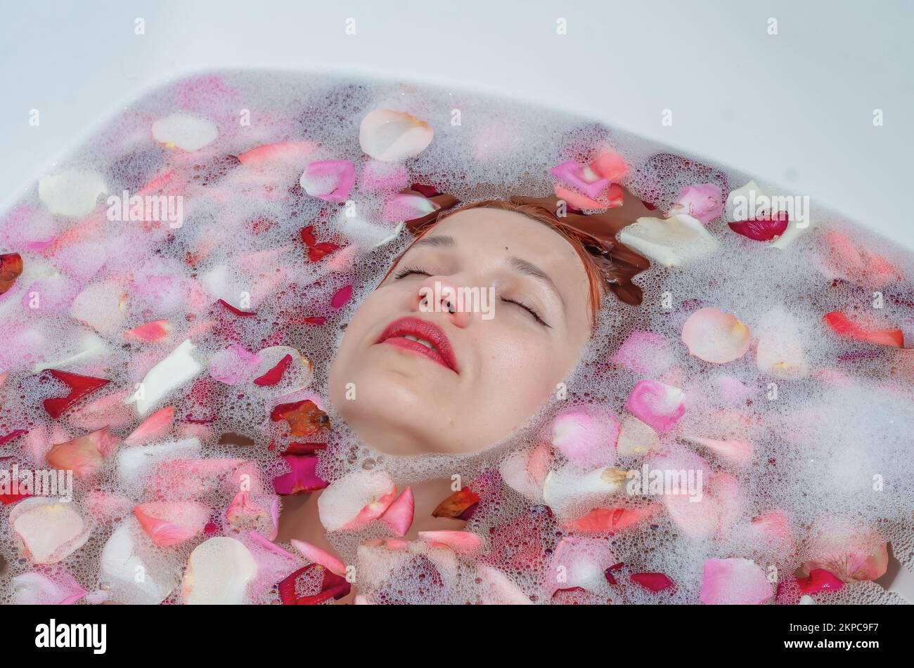 Close up female face in bath with soft white glowing and rose petals. Copyspace for advertising. Beauty, fashion, style, bodycare concept. Attractive Stock Photo
