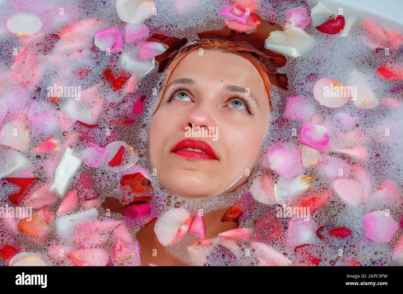 face of a beautiful woman in the bathroom among foam and rose petals Stock Photo