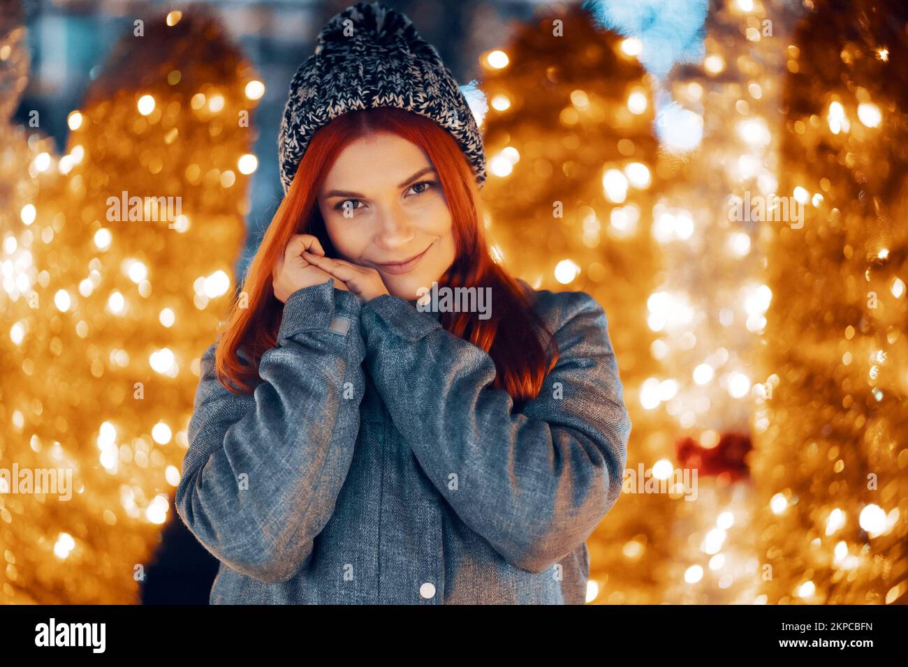 Outdoor night photo of young beautiful happy smiling girl enjoying festive decoration, posing in Christmas fair, in street of european city, wearing k Stock Photo