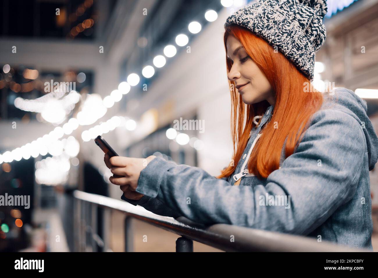 Beautiful Young Woman Using Smartphone Standing on the Night City Street Full of Light. Portrait of Gorgeous Smiling Female Using Mobile Phone. Stock Photo