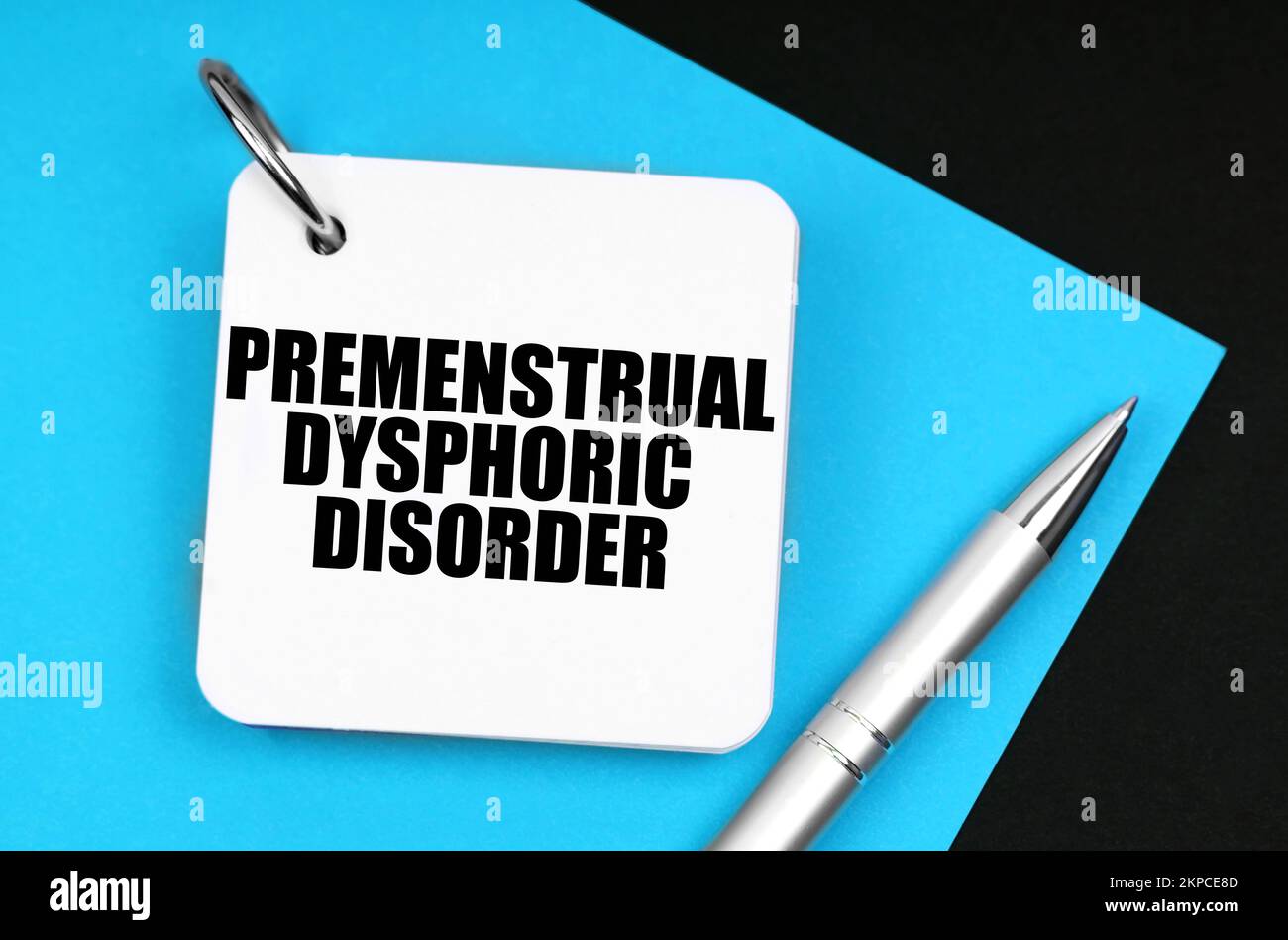 Medicine and health concept. On the black surface lies blue paper, a pen and a notebook with the inscription - Premenstrual Dysphoric Disorder Stock Photo