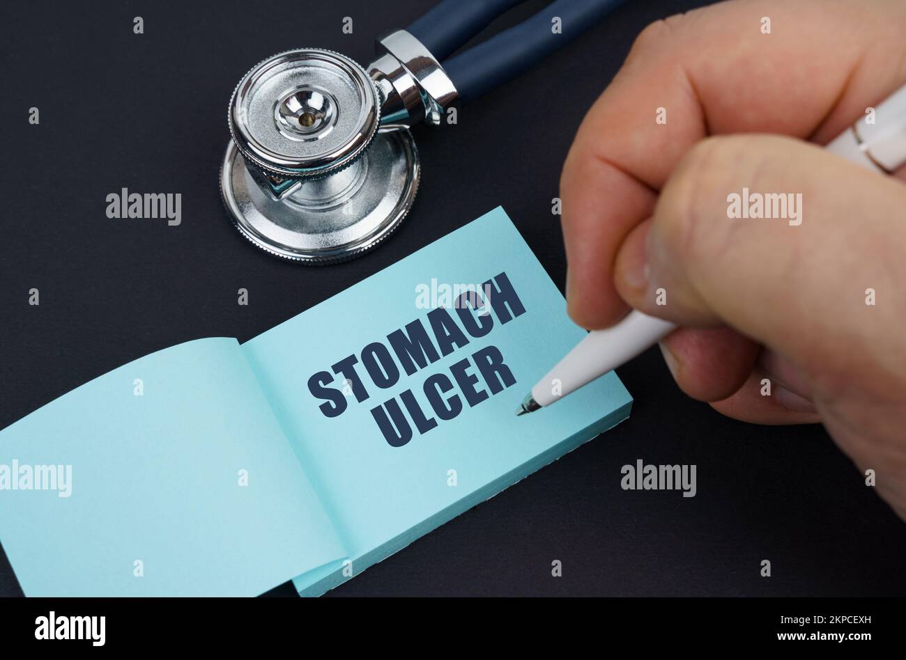 Medicine and health concept. On a black table is a stethoscope and a notebook in which the man wrote - STOMACH ULCER Stock Photo