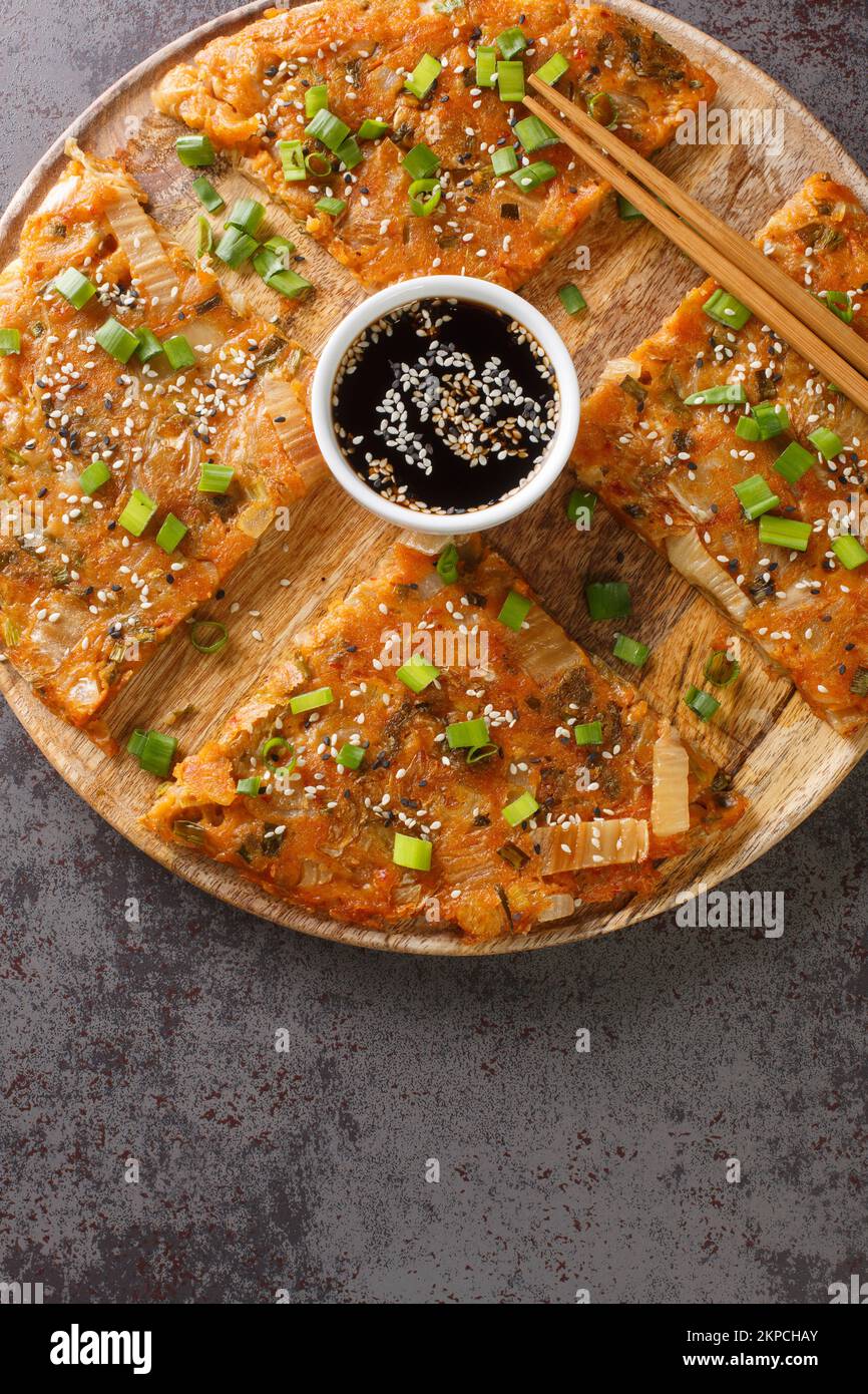 Korean style kimchi pancake Kimchijeon served with a dipping sauce and sprinkled with sesame and green onion closeup on the wooden board on the table. Stock Photo