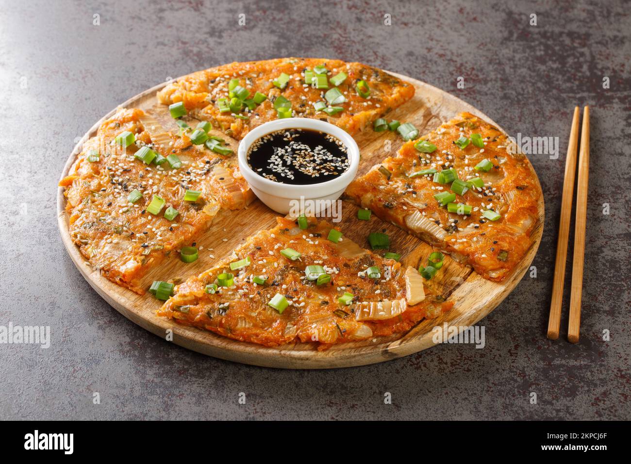 Kimchijeon is a Korean savory crispy pancake made of kimchi with flour and onion closeup on the wooden board on the table. Horizontal Stock Photo