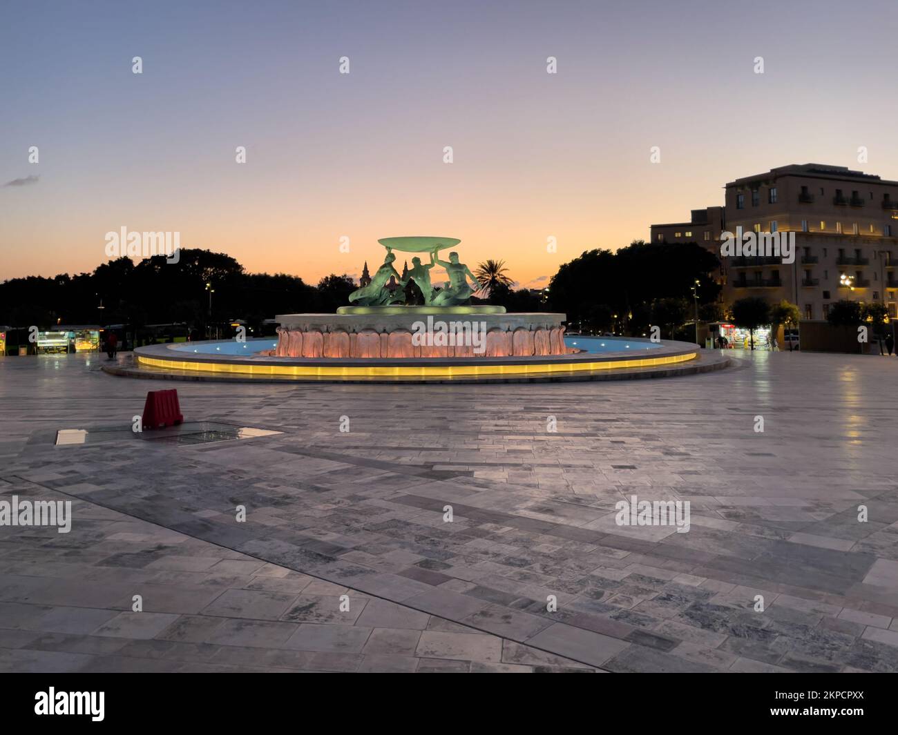 Triton Square, Valletta, Malta - January 11th 2022: The Triton Fountain lit in the evening with the remains off a golden sky in the background. Stock Photo