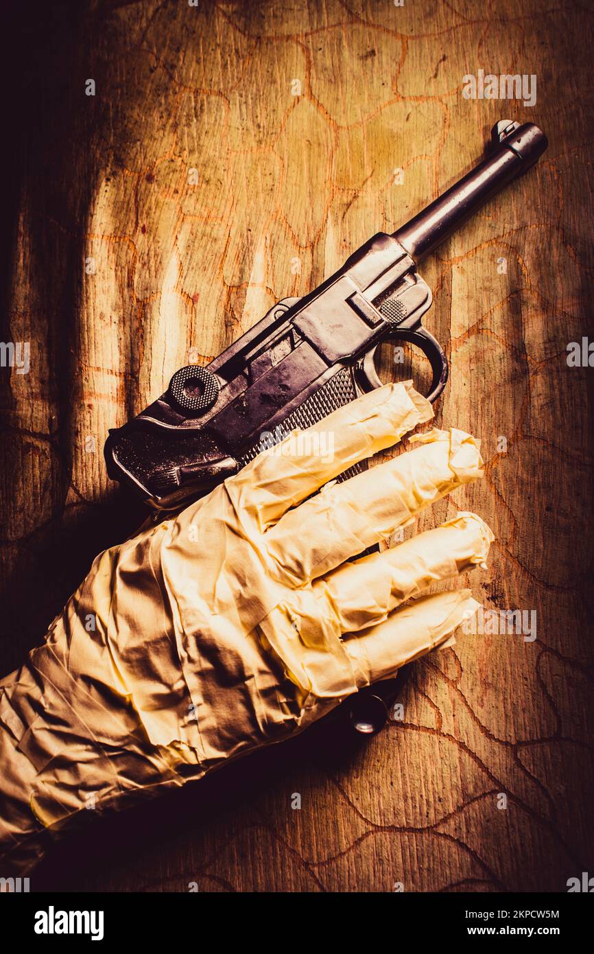 Closeup on a mummy hand holding gun against wooden wall. Curses of revenge Stock Photo