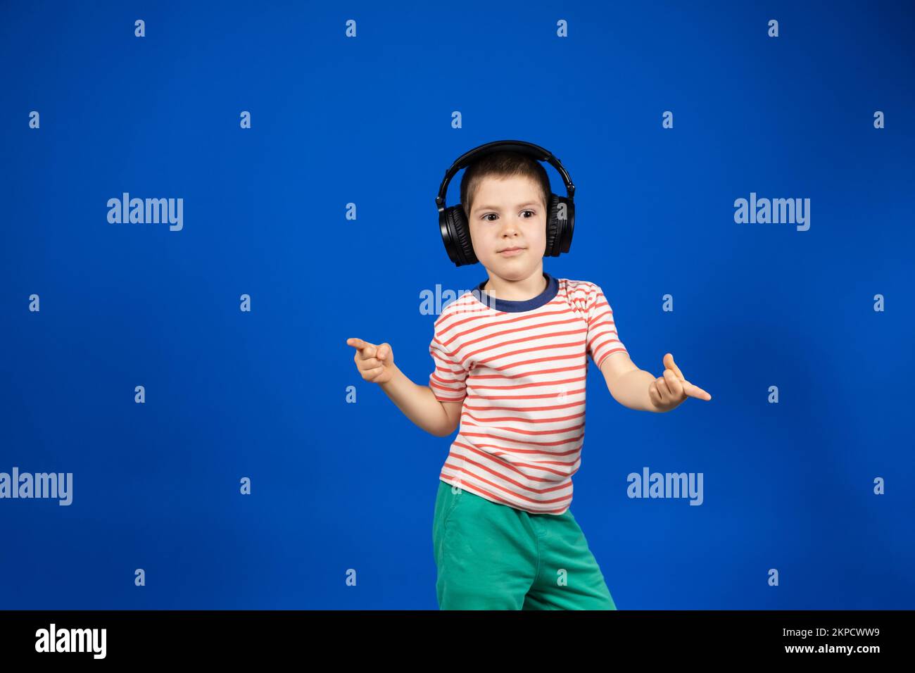 Happy smart 5 year old boy in big black headphones points fingers to the sides in place for text copy space Stock Photo