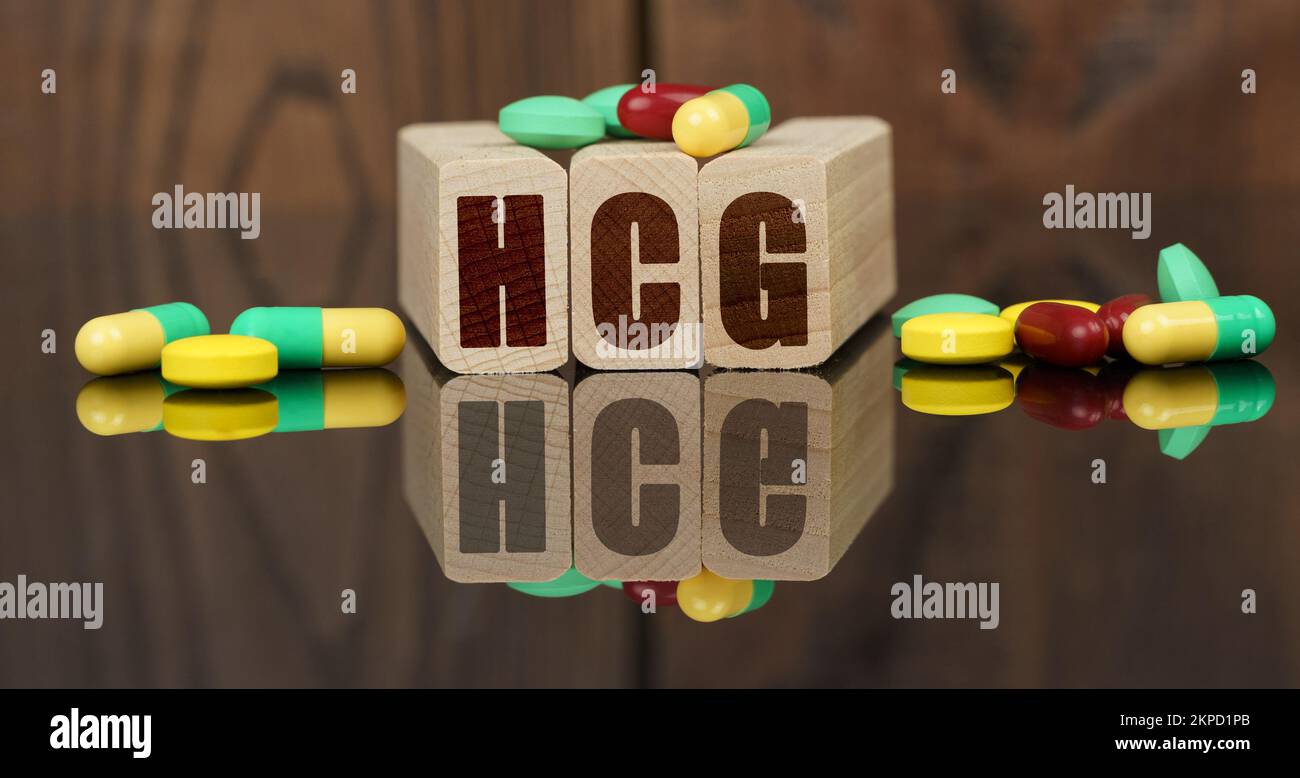 Medicine and health concept. On the surface are visible tablets, wooden dies and their reflections on which it is written - HCG Stock Photo