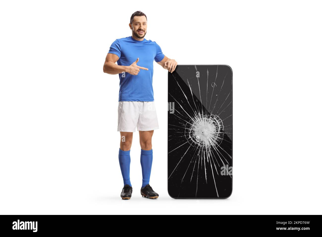 Full length portrait of a football player pointing at a big smartphone with broken screen isolated on white background Stock Photo