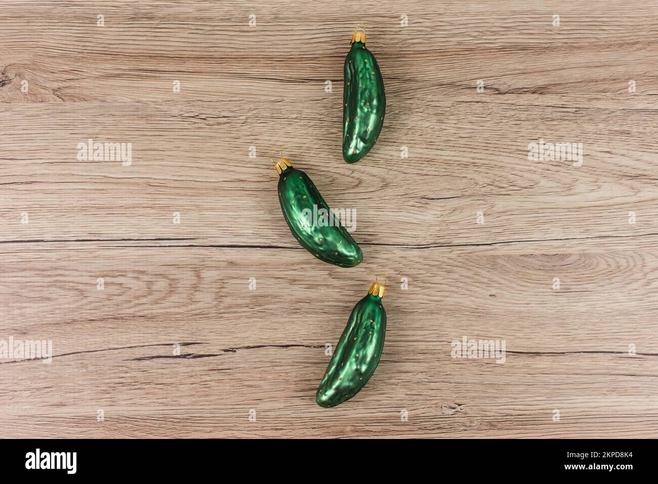 Three Christmas tree baubles in the shape of a cucumber are lying on a wooden background. Stock Photo