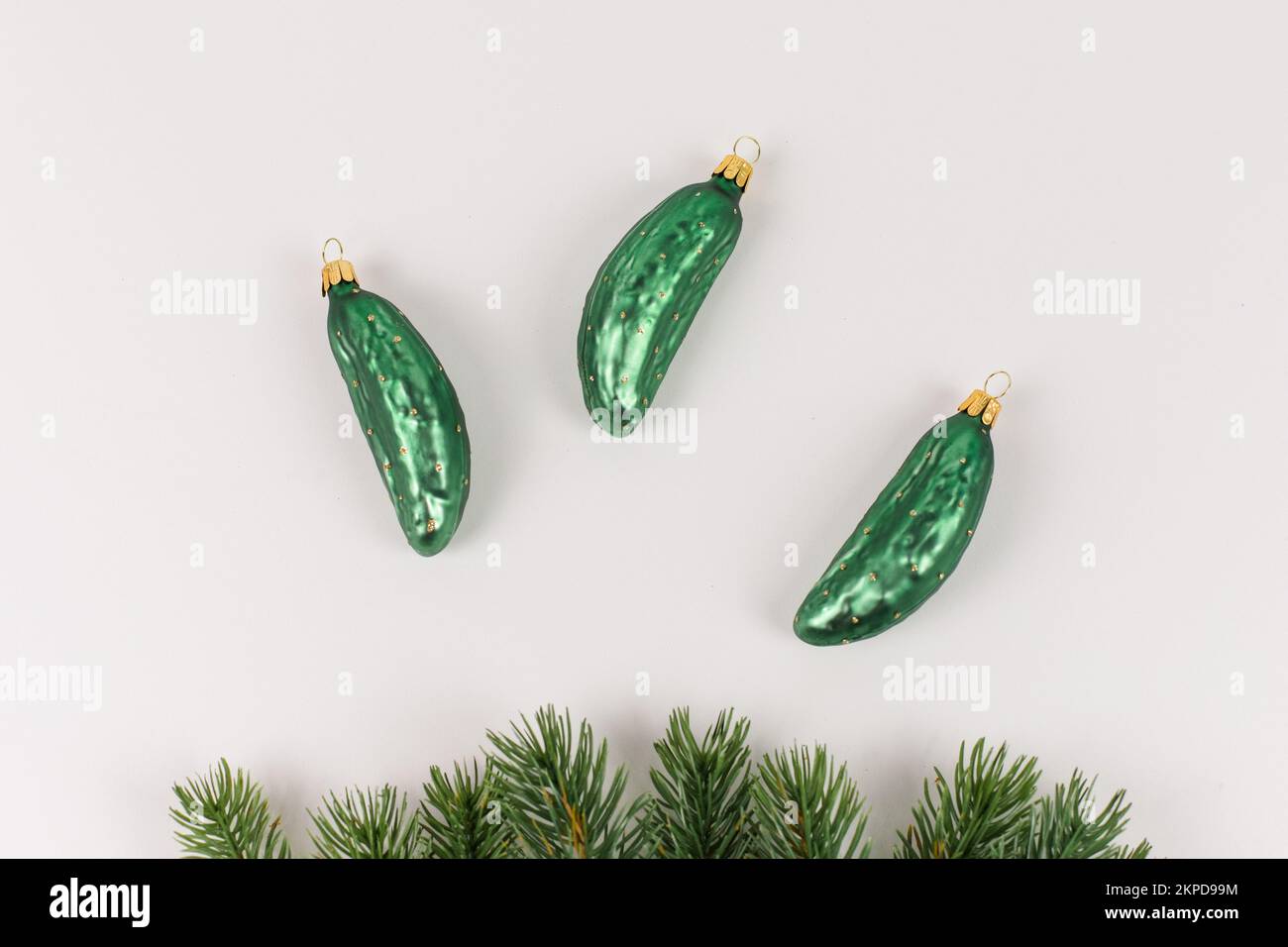 Three Christmas tree baubles in the shape of a cucumber are lying on a white background. Fir branches decorate the picture. Stock Photo