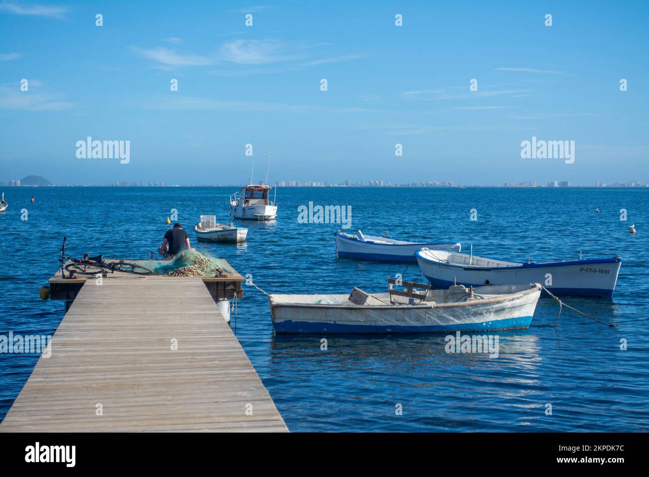 Fisherman sitting on the end of a jetty with fishing boats moared on the Mar Menor, Costa Calida, Murcia, Spain Stock Photo