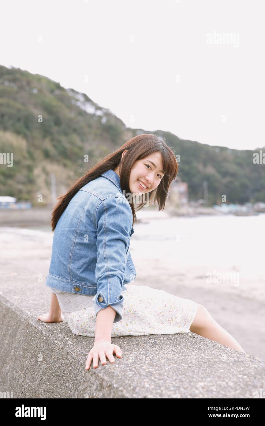Young Japanese woman sitting on the sea barrier Stock Photo - Alamy