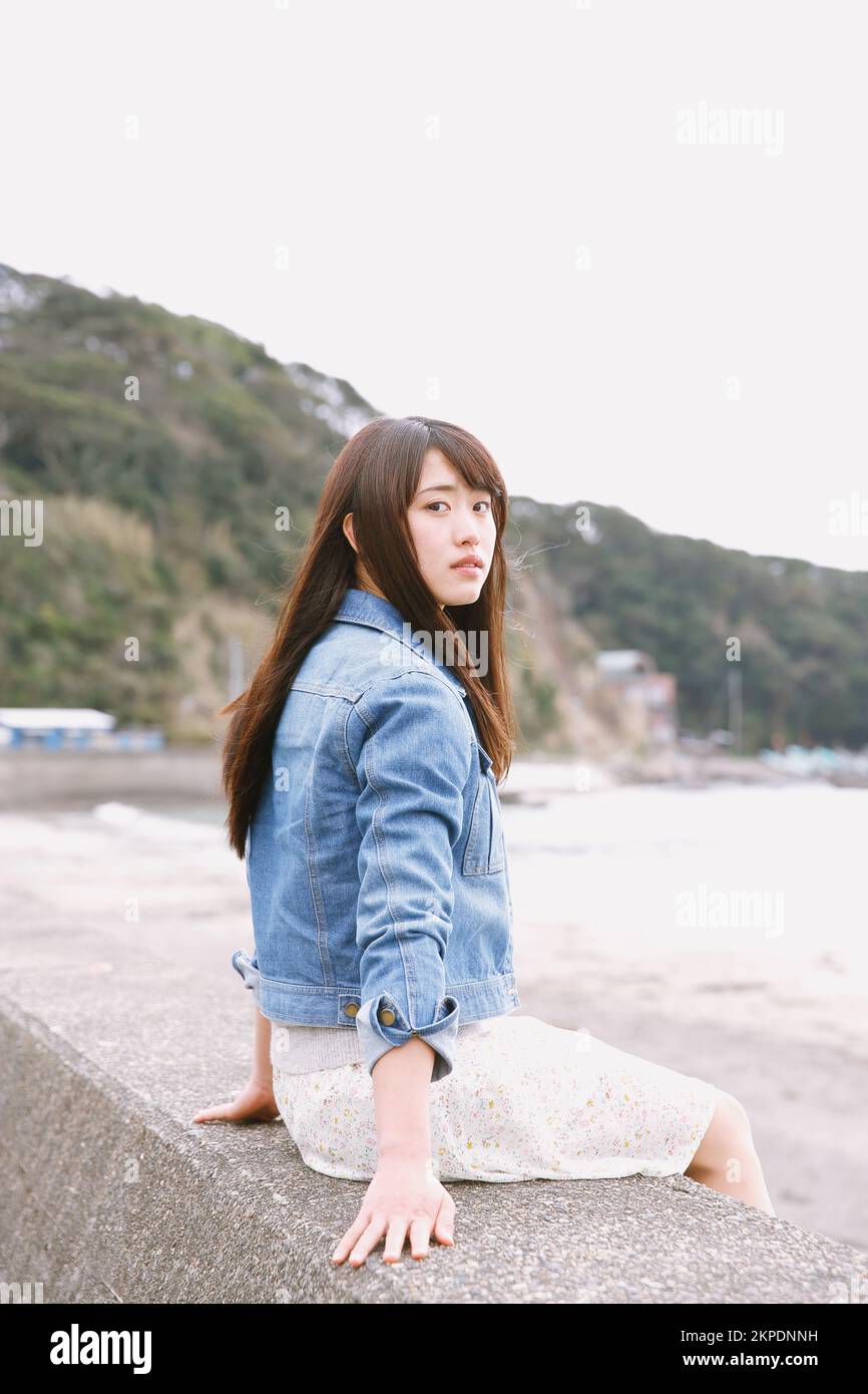 Young Japanese woman sitting on the sea barrier Stock Photo - Alamy