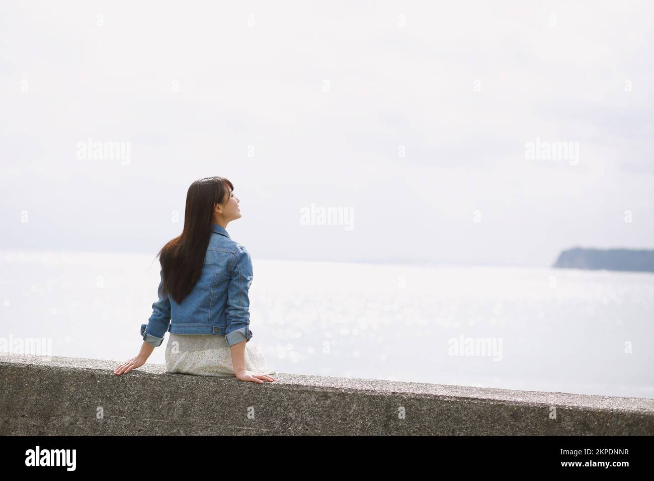Young Japanese woman sitting on the sea barrier Stock Photo - Alamy