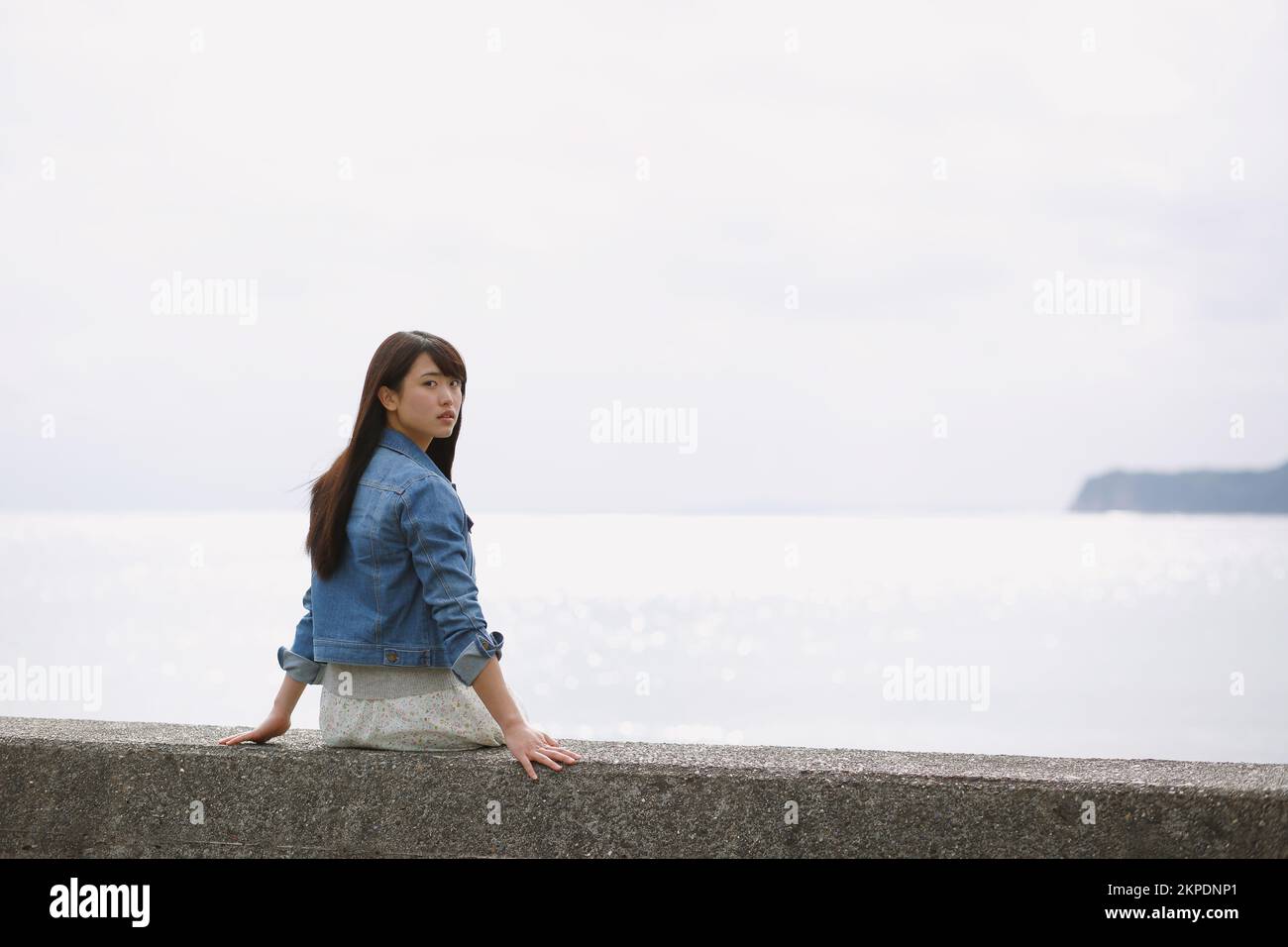 Young Japanese woman sitting on the sea barrier Stock Photo - Alamy
