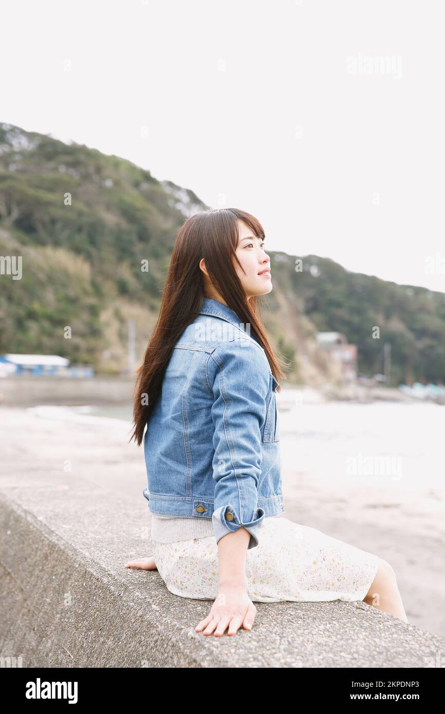 Young Japanese woman sitting on the sea barrier Stock Photo - Alamy