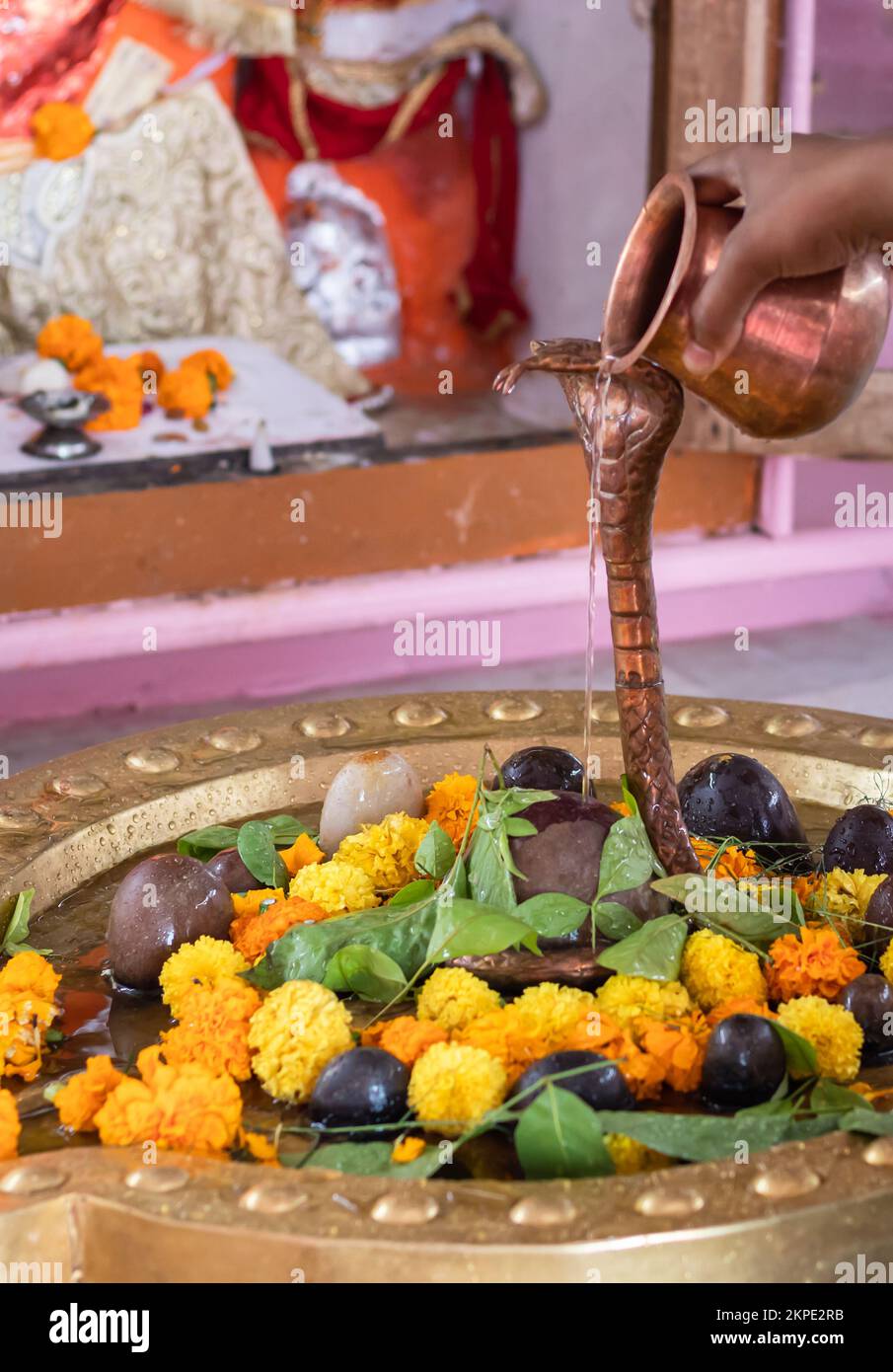 man offering holy water to hindu god shivalinga worshiped with flower and bell paper at temple Stock Photo