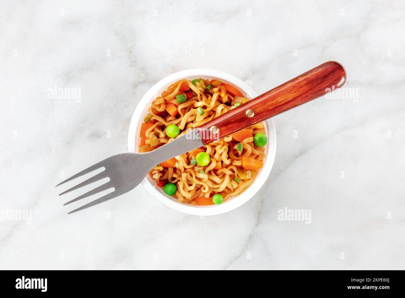 Ramen cup, instant soba noodles in a plastic cup with vegetables, green peas, onions, and carrots, top shot with a fork Stock Photo