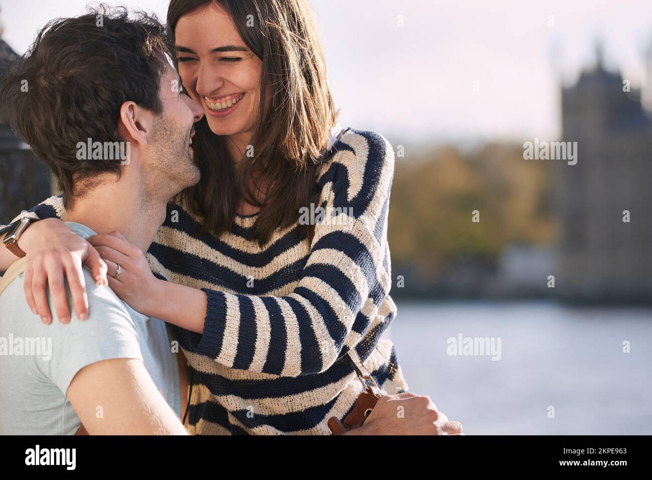 Love, travel and happy with couple in London for adventure, vacation and destination. Affectionate, hug and smile with man and woman in city at river Stock Photo