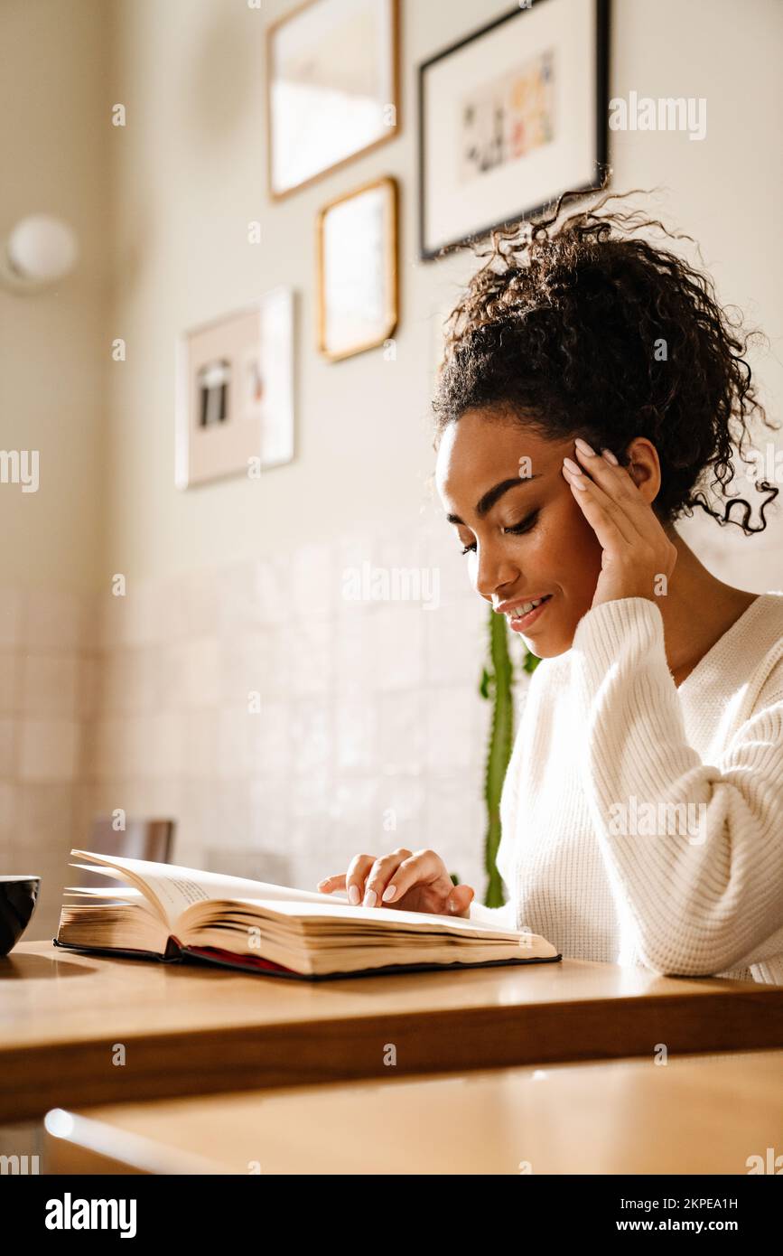 Young black woman smiling and reading book in cafe indoors Stock Photo ...