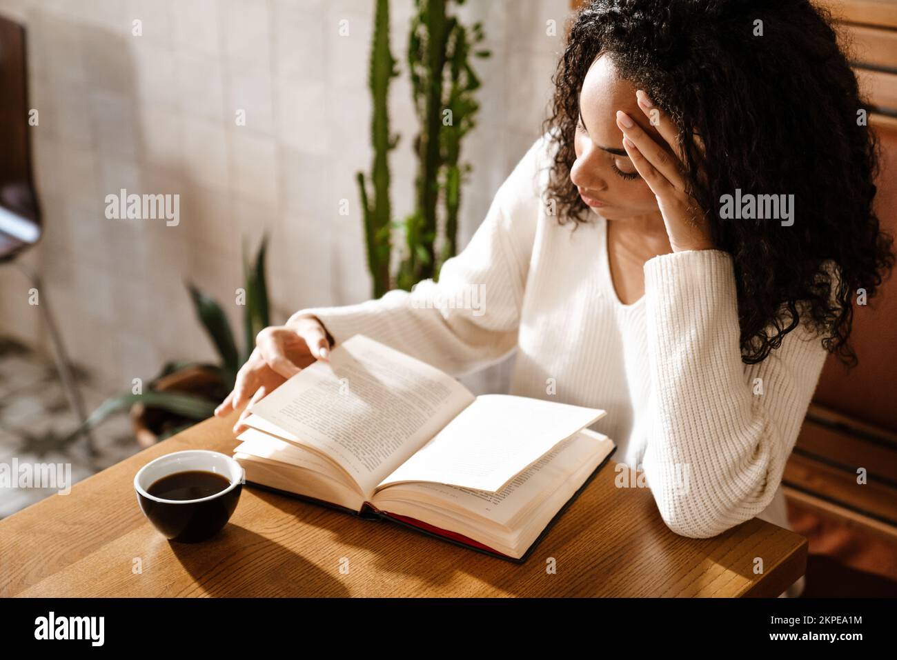 Young black woman drinking coffee and reading book in cafe indoors ...