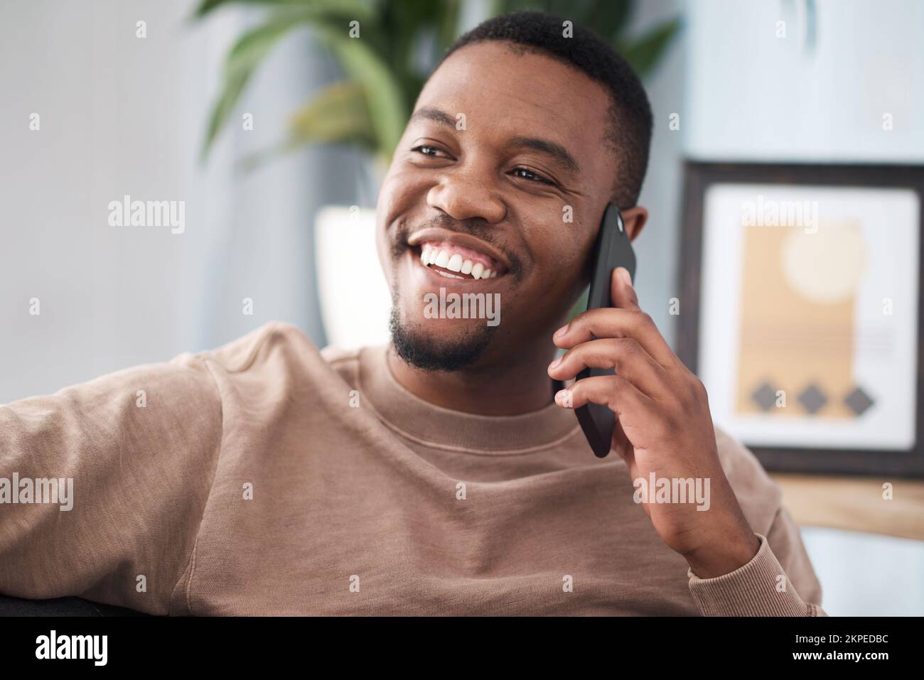 Black man, phone call and relax in home, house and living room, mobile communication and contact social network. Happy young african guy talking on Stock Photo