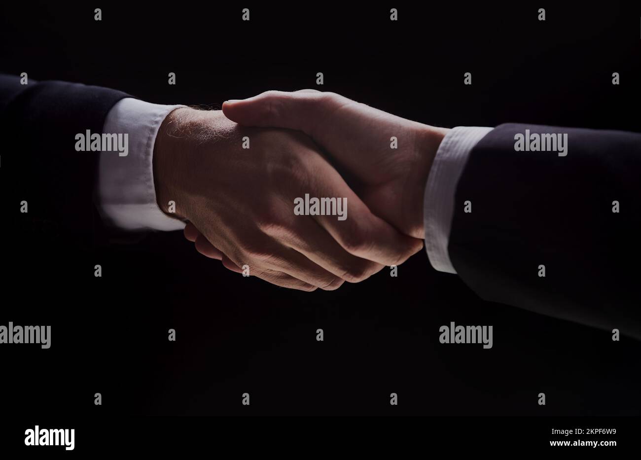 Photo of two men in suits shaking hands on a black background Stock
