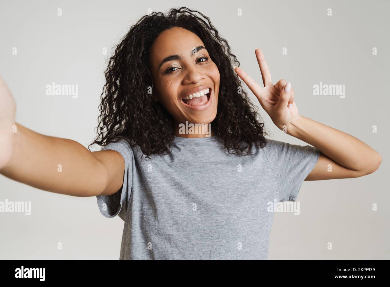 Young black woman showing peace sign while taking selfie photo isolated ...