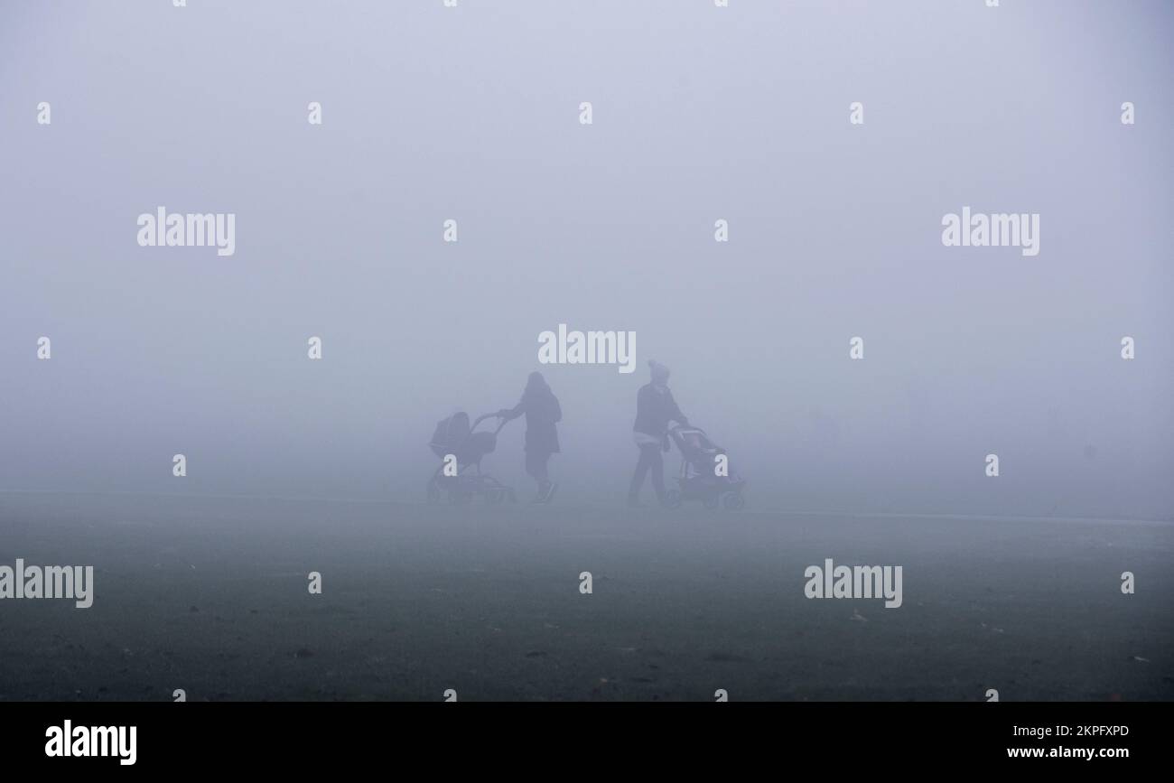 Harrogate, UK. 28th Nov, 2022. An eerie landscape was created by the fog on the Stray in the town centre this morning. two people with prams are silhoutted in the strange light. Picture Credit: ernesto rogata/Alamy Live News Stock Photo