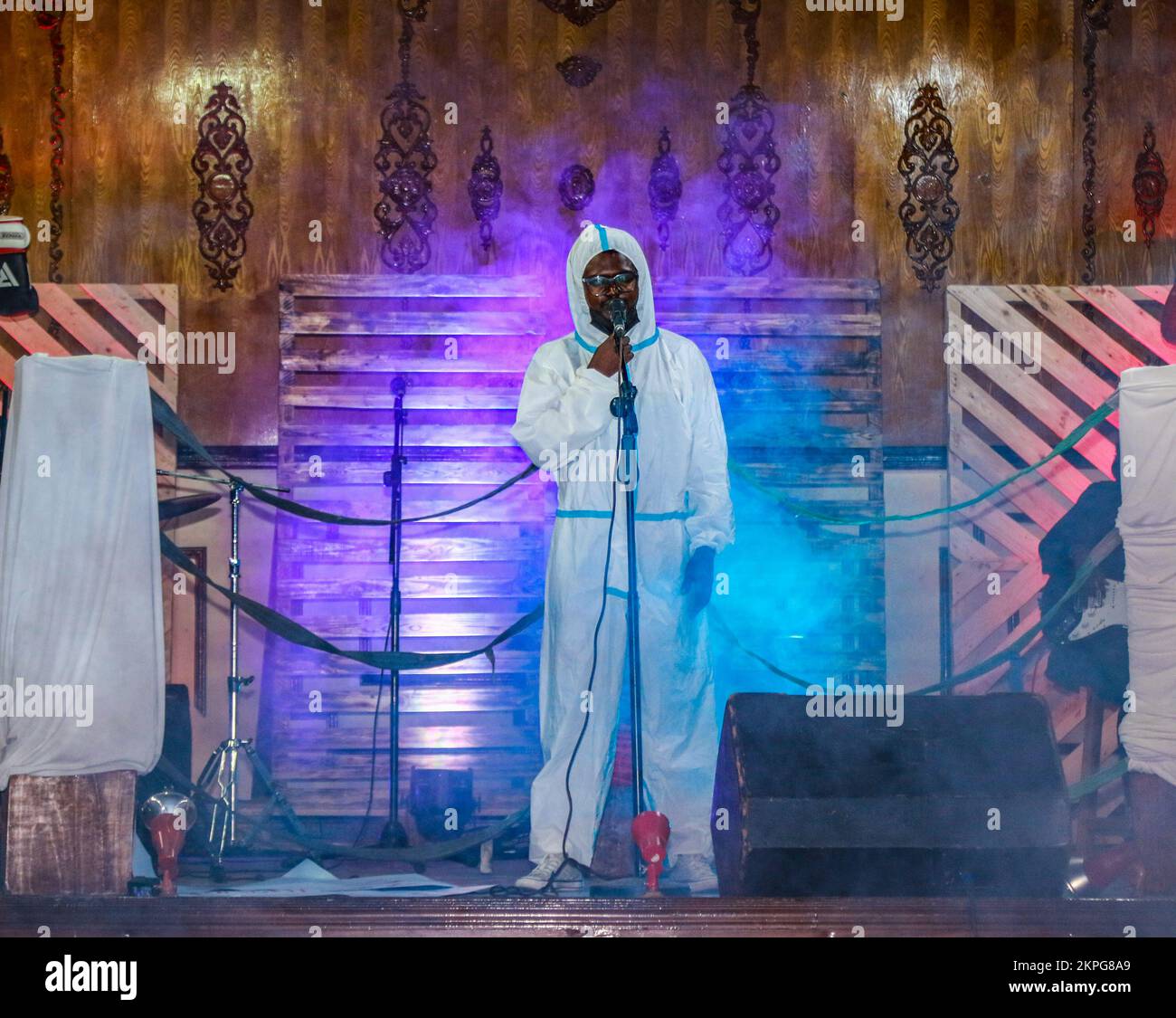 Nakuru, Kenya. 27th Nov, 2022. Spoken word artist Gregory Ochieng, who goes by stage name ''Mbunge Aliyeparara'' dressed in personal protective equipment (PPE) coverall, performs onstage during the release of his #Vitavyavina or ‘War of words' poetry album. Mbunge's poetry mainly highlights injustices and social issues in Kenya, among them, extrajudicial killings, profiling, government-sponsored enforced disappearances, and corruption, topics many regards as too risky to talk about. Credit: SOPA Images Limited/Alamy Live News Stock Photo