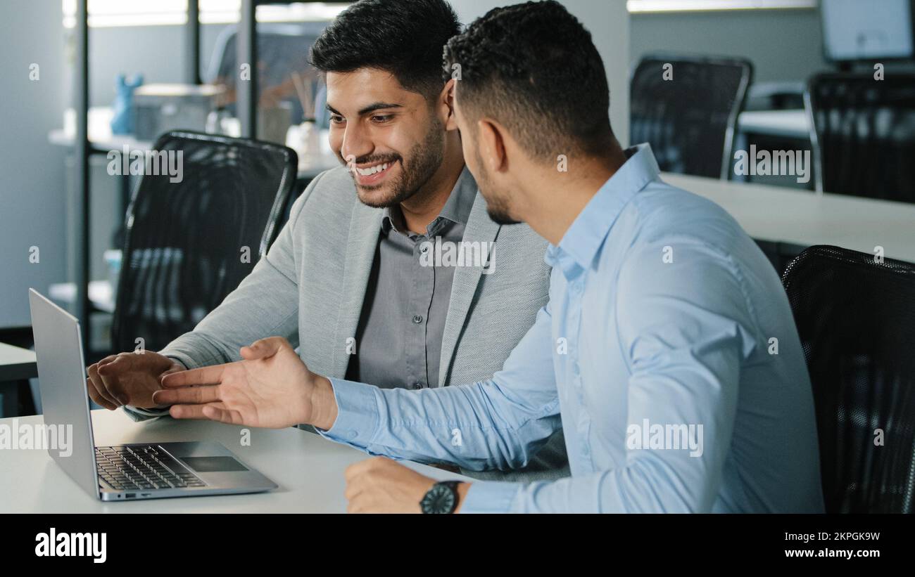 Two successful Arab male businessmen satisfied with result of negotiations, concluded contract. Smiling young colleagues Indian employees sitting in Stock Photo