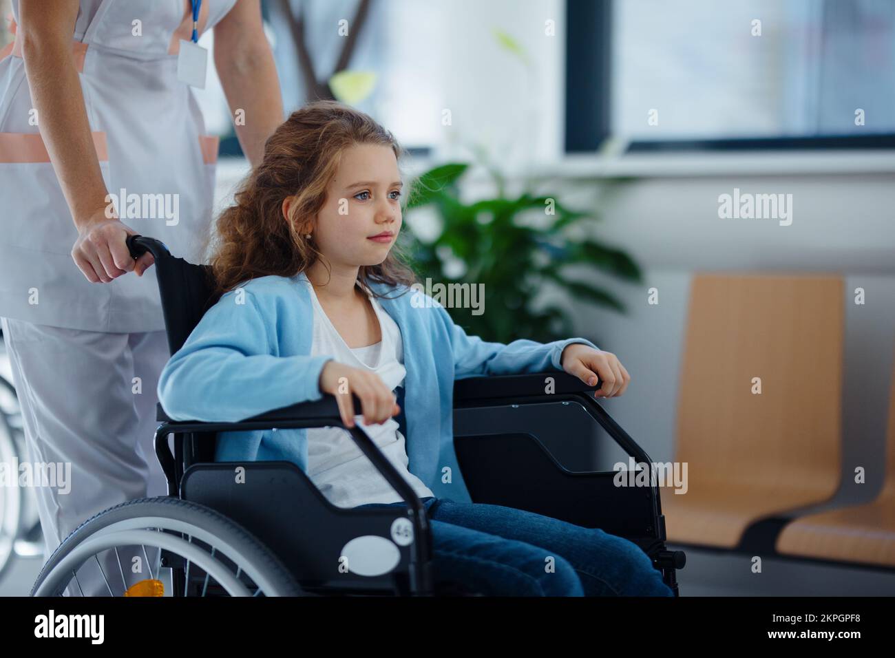 Nurse pushing little girl on wheelchair at hospital corridor. Stock Photo