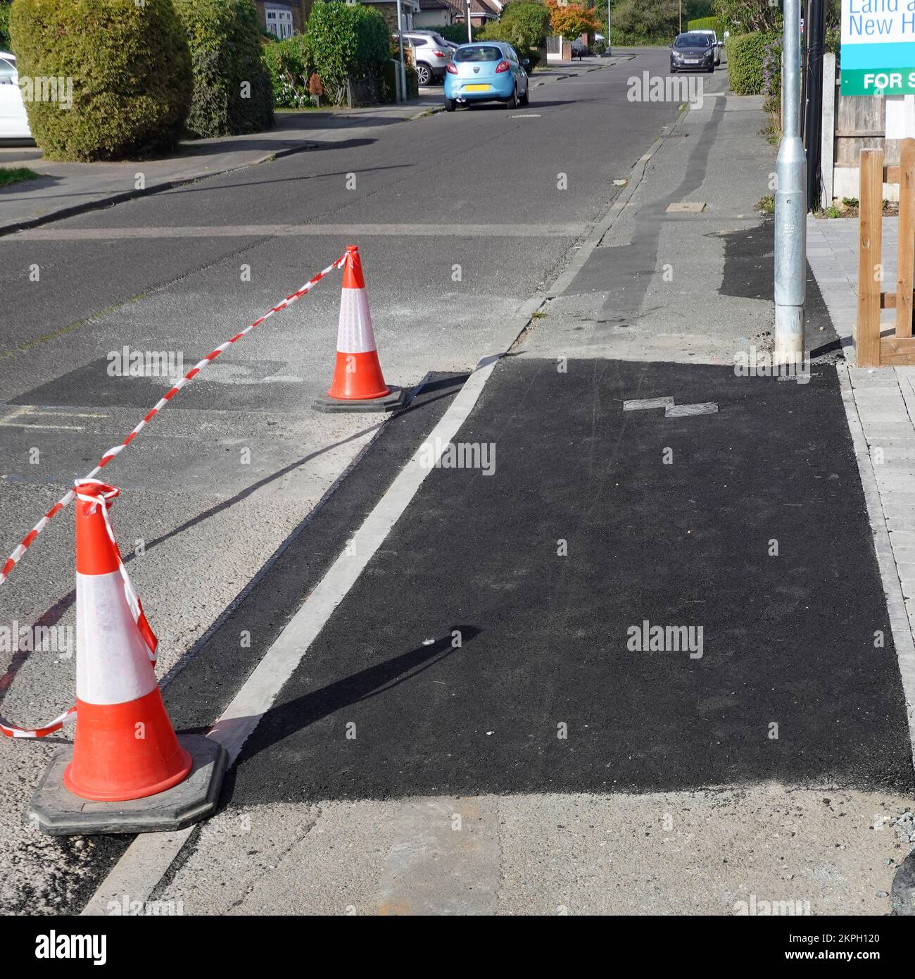 Coned off new pavement footway for vehicle crossover to new home property consists of dropped kerb concrete sub base & tarmac topping Essex England UK Stock Photo