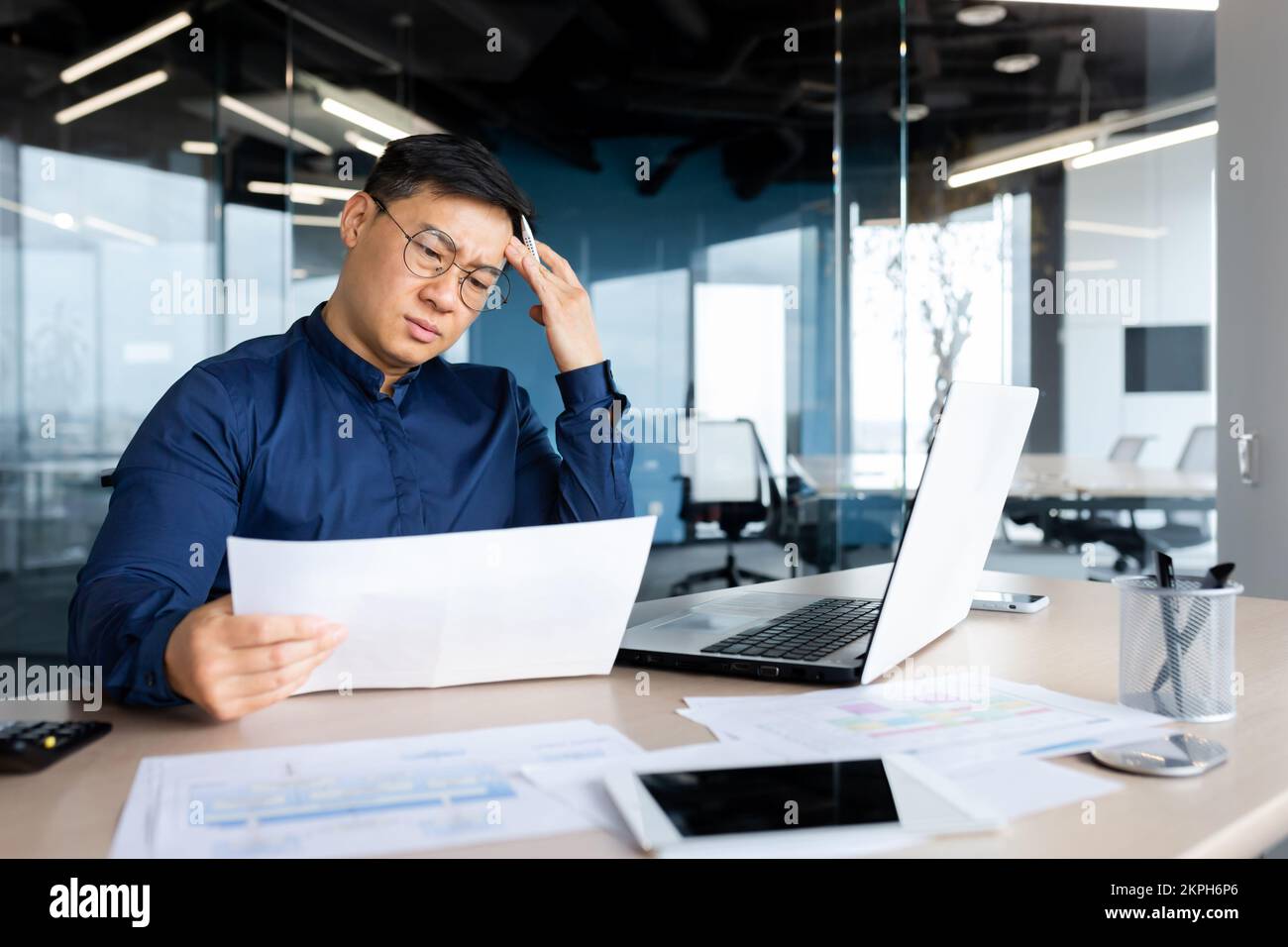 Desperate businessman looks and reads financial reports and documents, Asian boss works with documents inside office, confused and depressed. Stock Photo