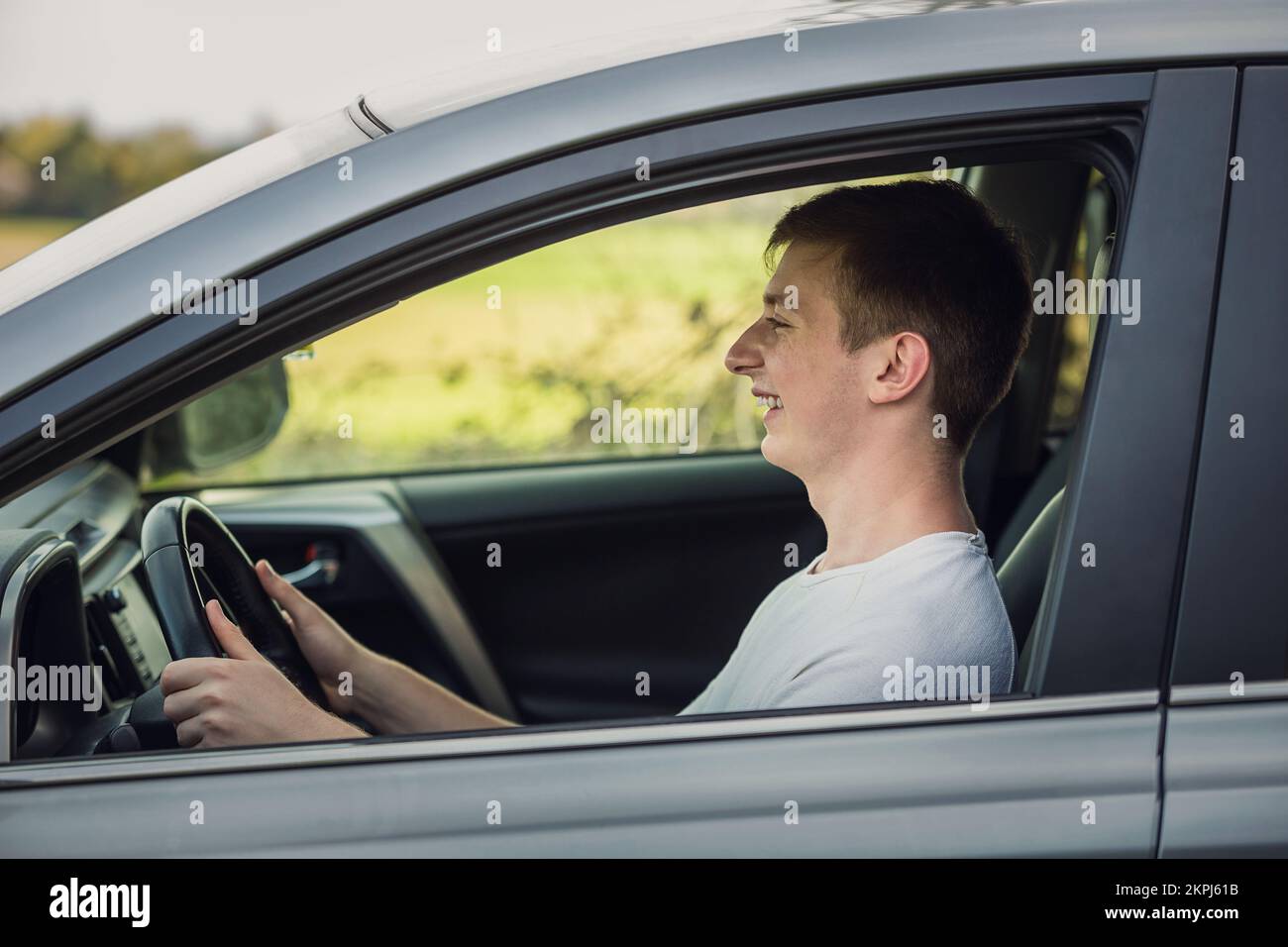 Joyful young man driving safe his new car, looking ahead at the street