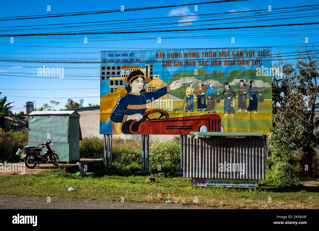 A Vietnam Communist Party painted propaganda billboard depicting ethnic minority people playing gfongs and driving a tractor.  The billboard urges peo Stock Photo