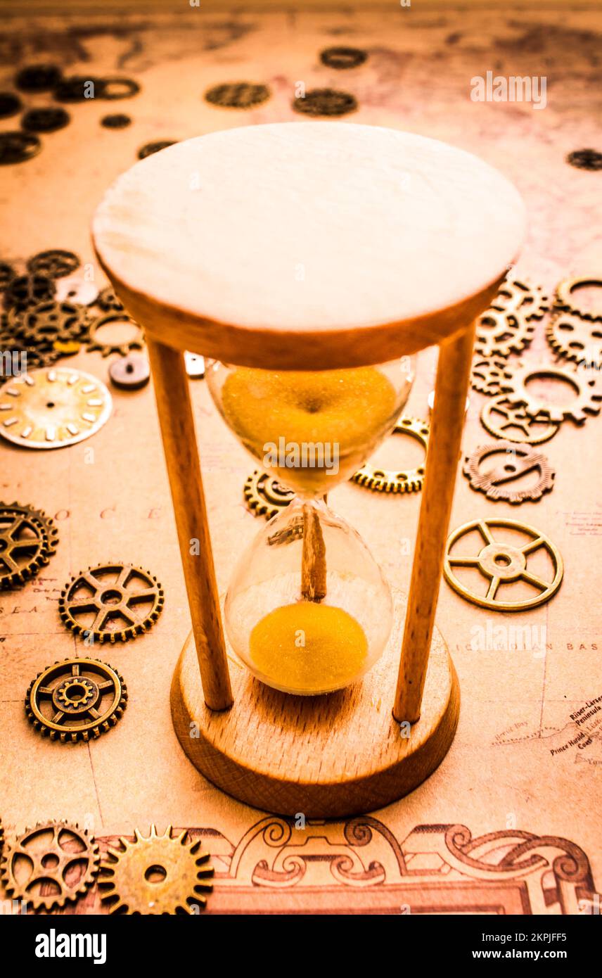 Old wooden hourglass clock surrounded by vintage watch gears and cogs