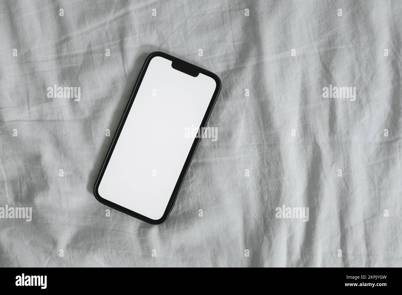 Smart mobile phone with blank mockup screen on wrinkled bed linen, top view Stock Photo