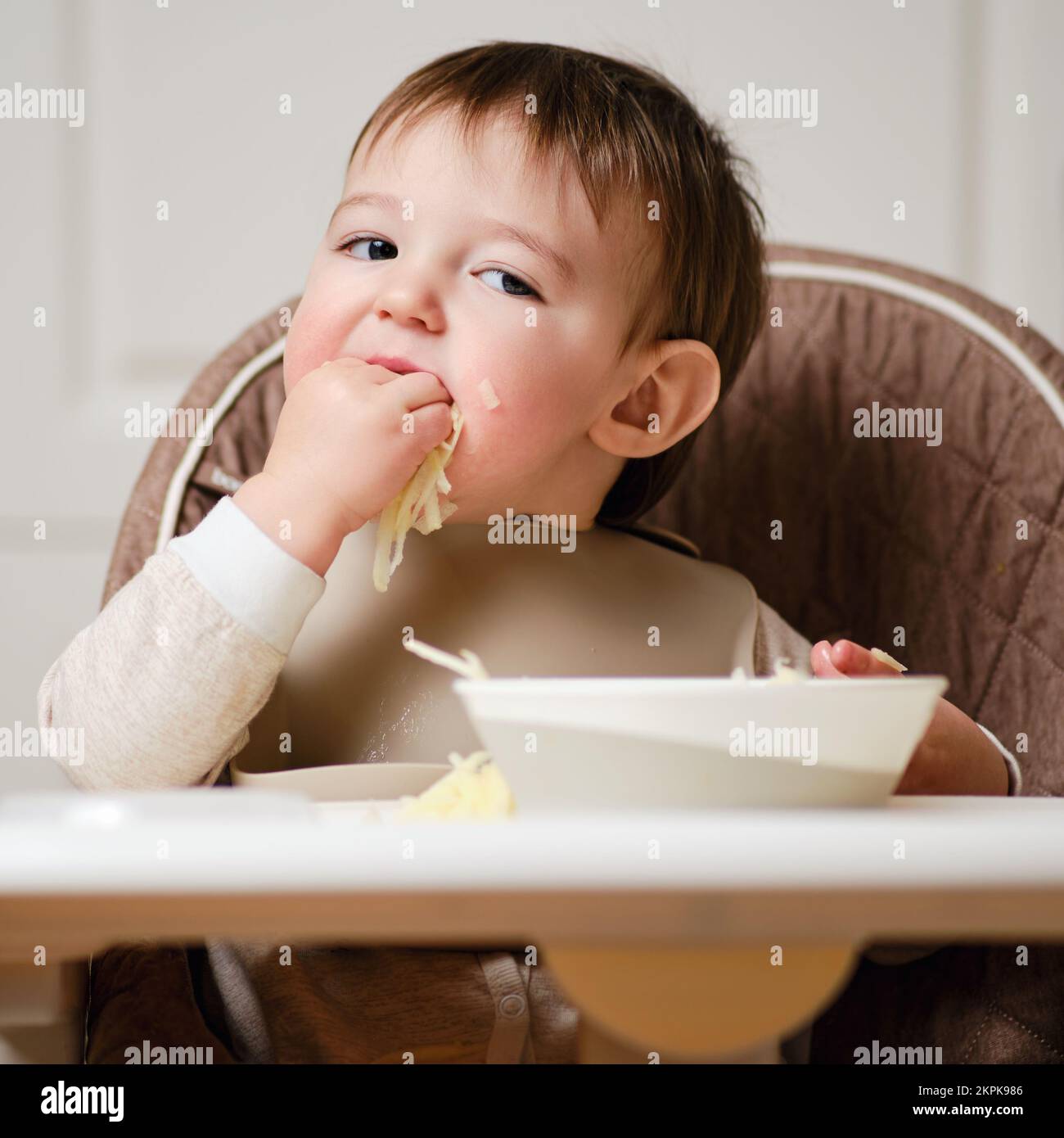 A funny child is eating a grated apple with his mouth full while