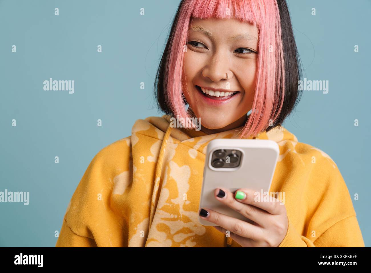 Asian girl with pink hair smiling and using mobile phone isolated over blue background Stock Photo