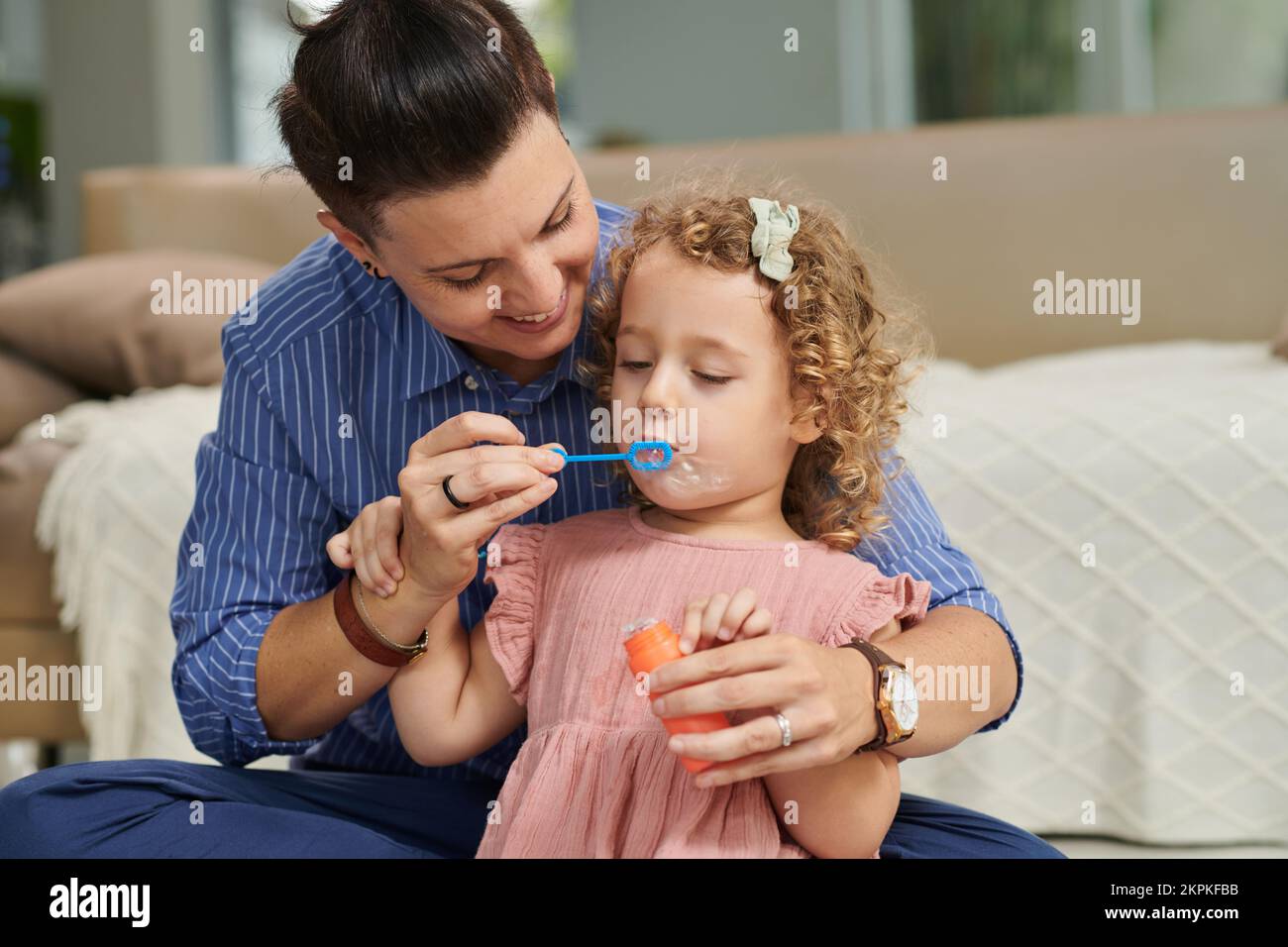 Joyful girl blowing soap bubbles for the first time, mother explaining how to do it right Stock Photo