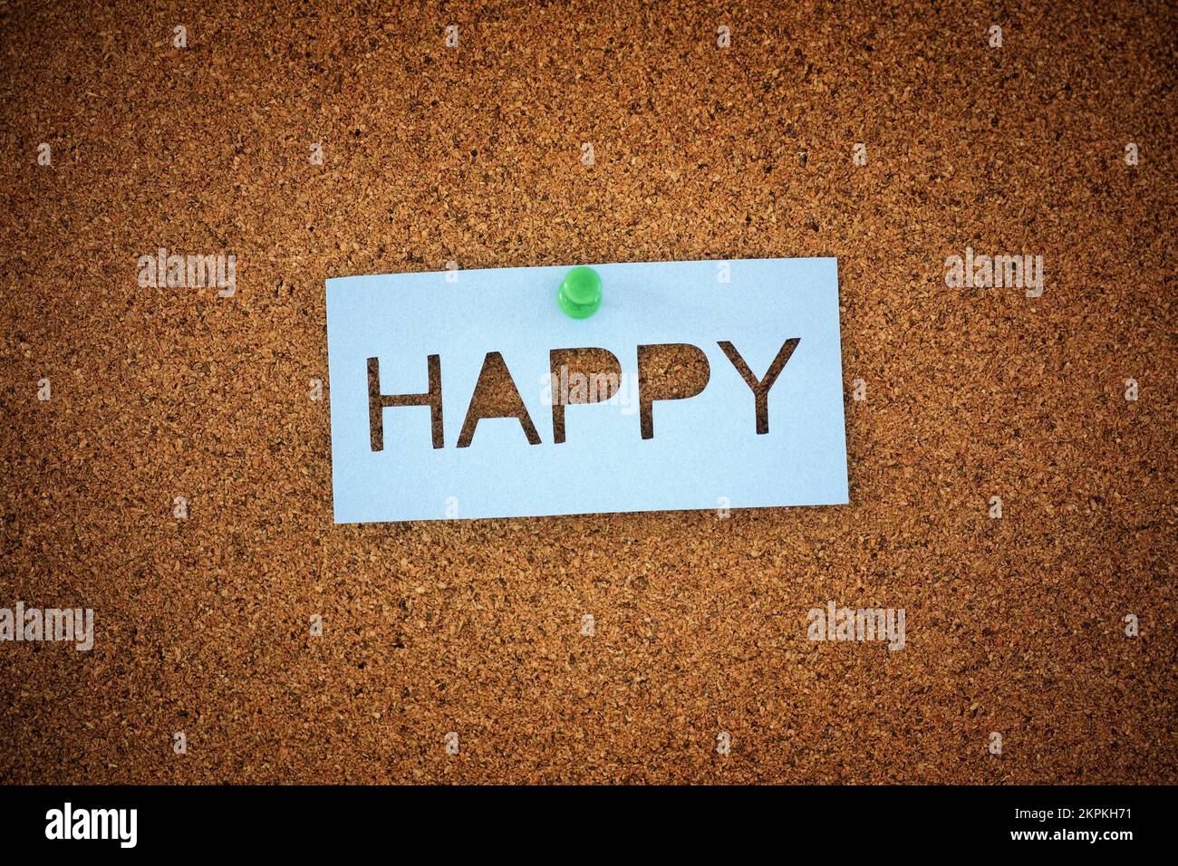The word Happy pinned to a cork board. Close up. Stock Photo