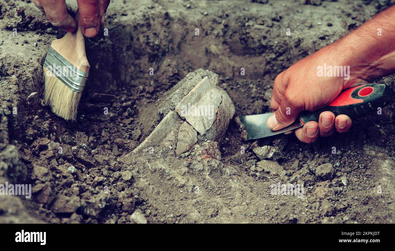 Archaeological excavations, archaeologists work, dig up an ancient clay artifact with special tools in soil Stock Photo